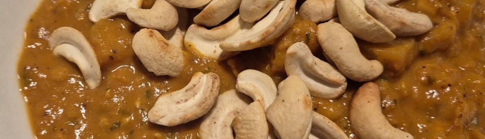 Teller mit Suppe aus Sellerie, Tomate Linsen udn Cashewkernen drauf