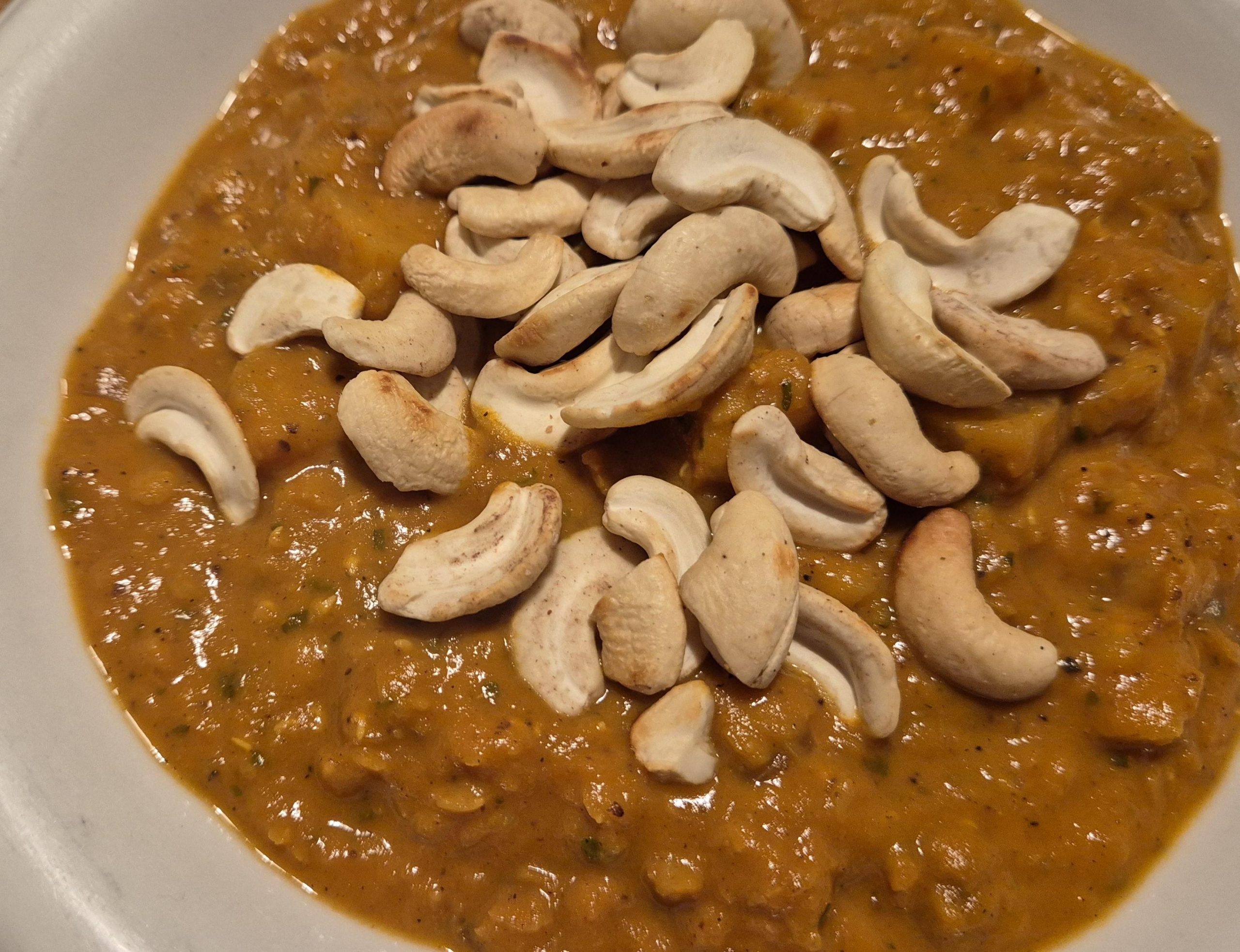 Teller mit Suppe aus Sellerie, Tomate Linsen udn Cashewkernen drauf